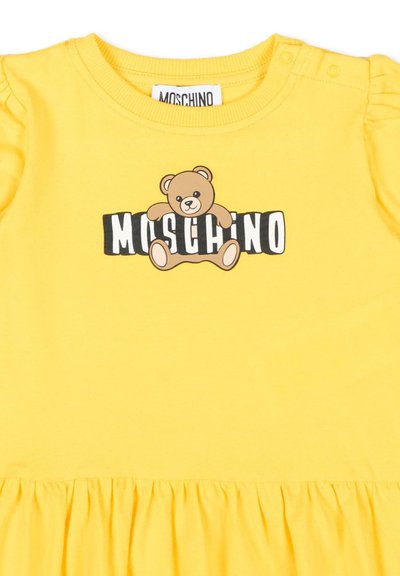 Geel peuterjurkje met pofmouwen en een teddybeerafbeelding boven het woord "Moschino" op de borst.