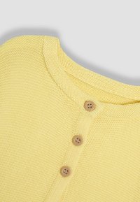 Maglione giallo a maglia con scollo rotondo, tessuto testurizzato e tre bottoni in legno sulla patta frontale.