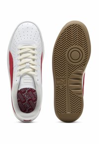 Sneakers bianche con accenti rossi, tomaia in pelle liscia, dettagli perforati, lacci piatti e suola in gomma con trazione a spina di pesce.