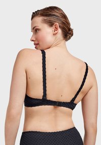 Brassiere nera con texture, spalline sottili e regolabili, chiusura a gancio e occhiello sul retro e un motivo a pois che copre il tessuto.
