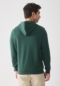 Groene hoodie van een zachte stof, met lange mouwen en een buidelzak. Heeft een aantrekkoord capuchon en ribgebreide onderrand en boorden.