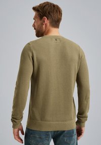 Olivgrüner gestrickter Pullover mit strukturierter Musterung, Rippbündchen und Saum, ausgestattet mit einem kleinen Emblem am hinteren Halsausschnitt.