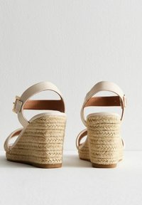 Sandales à talons compensés en simili cuir beige clair avec un talon en jute tissé. Elles présentent une bride de cheville réglable et une semelle plateforme plate.
