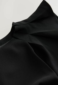 Tissu noir à la texture lisse et au design drapé. Présente des plis doux le long de l'encolure, créant une silhouette fluide.