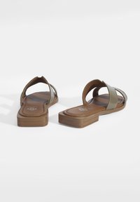 Des sandales plates avec des brides vert olive, un design à bout ouvert et une semelle intérieure marron rembourrée. Elles possèdent un talon bloc léger et discret.