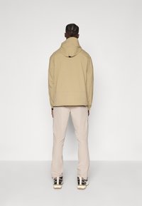 Beige huppari, kevyt materiaali, hieman ylisuuri malli. Vaaleanpunaiset housut ja musta-valkoiset kengät. Siisti, minimalistinen muotoilu.