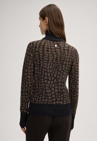 Gestrickter Pullover in Braun und Schwarz mit einem strukturierten Gittermuster, hohem Kragen und gerippten Bündchen. Verfügt über einen silbernen Akzent auf der Rückseite.