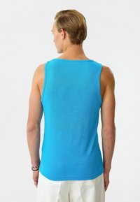 Blauwe katoenen tanktop met een ronde hals en zonder mouwen. De stof heeft een soepele textuur en een aansluitende pasvorm, die de rug accentueert.