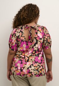 Blommig blus med svart bakgrund, med stora mönster i rosa och orange, korta puffärmar och en knytning på baksidan.