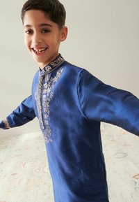 Kurta blu a maniche lunghe realizzato in tessuto testurizzato, con ricami dorati sul colletto e sulla parte frontale, caratterizzato da intricati motivi floreali e fogliari.