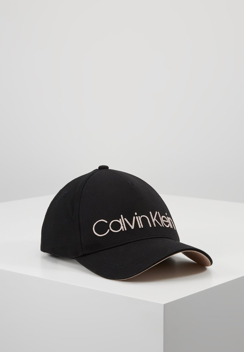 Casquette de baseball noire à visière incurvée avec le logo "Calvin Klein" brodé en blanc sur le panneau avant, exposée sur une surface blanche.