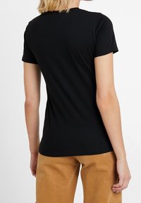 Camiseta negra de manga corta con un diseño ajustado, textura suave y cuello redondo. Presenta un estilo simple y limpio sin logotipos visibles.
