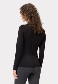 Schwarzes Langarmoberteil mit körpernahem Design und glatter Textur, mit einer Nahtdetails auf der Rückseite. Kombiniert mit grauen Leggings.