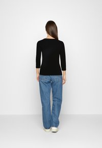 Schwarzes enges Oberteil mit Dreiviertelärmeln, kombiniert mit lockeren hellblauen Jeans und weißen Turnschuhen, von hinten betrachtet.