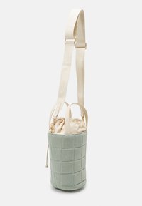 Pikowana jasna zielona torba typu bucket z kremowym zamknięciem na ściągacz, regulowanym paskiem i złotymi detalami. Zewnętrze z fakturowanej tkaniny.