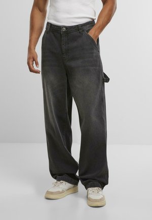 Loose-fitting dark gray denim pants with a button closure, front pockets, and a side loop detail, paired with white and beige sneakers.