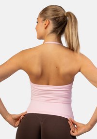 Jasnoróżowy dopasowany top na ramiączkach z bezszwowym wykończeniem i dekoltem na halter, wykonany z miękkiego materiału o gładkiej fakturze. Widok z tyłu ukazuje minimalistyczny styl.