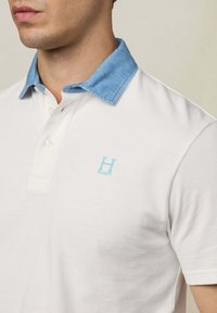 Weiße Polohemd mit einem Kragen im Jeansstil; verfügt über ein gesticktes blaues "H"-Logo auf der Brust; strukturierter Stoff.