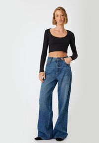 Maglietta nera a maniche lunghe e corta abbinata a jeans blu a vita alta e gamba larga. Texture liscia con un classico lavaggio denim e un leggero scolorimento.