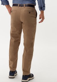 Pantaloni in cotone beige con taglio dritto, dotati di due tasche posteriori e una cintura in pelle nera, abbinati a sneakers navy.