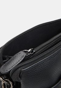 Borsa in pelle nera con chiusura a zip, superficie texturizzata e dettagli in metallo. L'interno è foderato con un tessuto liscio.