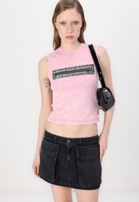 Rausvai klasikinė be rankovių crop top su juodu užtrauktuku; derinama su trumpa juoda džinsine sijonkleite, kuri turi dideles priekinės kišenes.