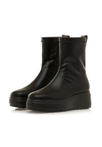Botas negras de cuero hasta el tobillo con un acabado suave y brillante. Cuentan con una suela gruesa y plataforma, además de paneles laterales elásticos para facilitar su uso.