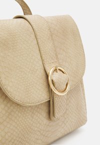 Bolso beige con patrón texturizado de piel de serpiente. Presenta una solapa redondeada y un cierre con anillo dorado. Acabado liso con una forma estructurada.