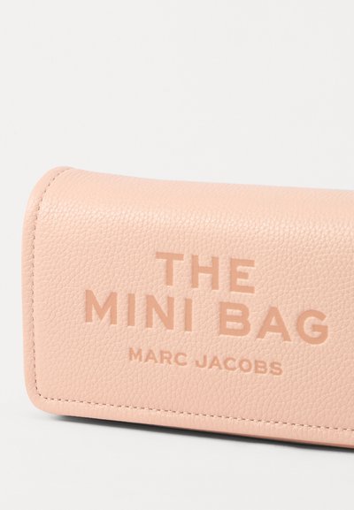 Roosa nahast mini kott, millel on debosseeritud tekst "THE MINI BAG" ja "MARC JACOBS." Sile tekstuur, ümarad servad ja nähtav õmblus.