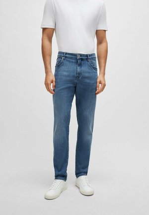Jeans en denim bleu clair avec une coupe droite, cinq poches et une fermeture à bouton, associés à un t-shirt blanc uni et des baskets blanches.