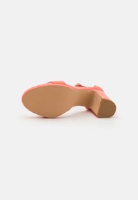 Coral closed-toe heel with a textured rubber sole, featuring a gold buckle on the strap and a wide, sturdy heel for support.
