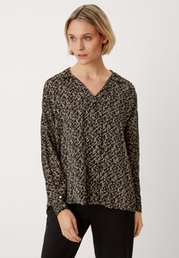 Blusa nera con scollo a V e maniche lunghe, decorata con un motivo geometrico color sabbia su tutta la superficie. Tessuto morbido e leggero.