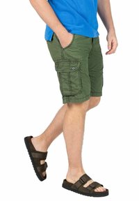 Grüne Cargo-Shorts mit Seitentaschen und Knopfverschluss, kombiniert mit braunen Sandalen mit verstellbaren Riemen und einer strukturierten Sohle.