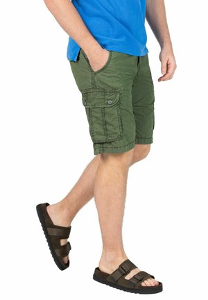 Green cargo shorts with side pockets and button closures, paired with brown sandals featuring adjustable straps and a textured sole.