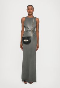Abito maxi grigio senza maniche con design attorcigliato in vita. Abbinato a una borsa a tracolla nera con dettagli dorati e indossato con sandali aperti.