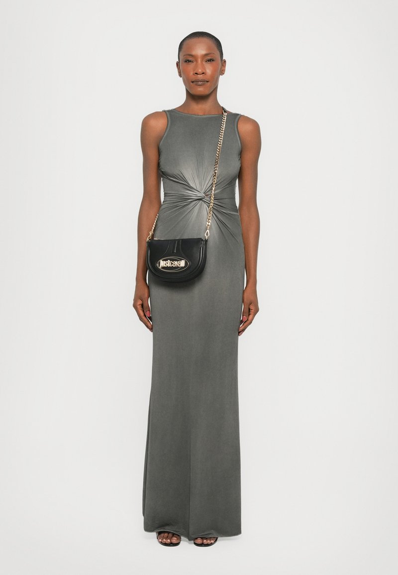 Abito maxi grigio senza maniche con design attorcigliato in vita. Abbinato a una borsa a tracolla nera con dettagli dorati e indossato con sandali aperti.