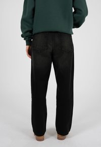 Pantaloni negri din denim cu croială lejeră, având talie medie, buzunare pe spate cu detalii de cusături și o talie simplă.