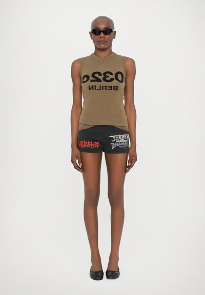 Top senza maniche marrone con "0320 BERLINO" in nero, abbinato a pantaloni corti neri con testo grafico rosso e bianco, e ballerine nere.