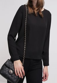 Zwart long-sleeve top met een ronde halslijn, gecombineerd met een zwart gewatteerde handtas met een kettinghengsel en een decoratieve hardware accent.
