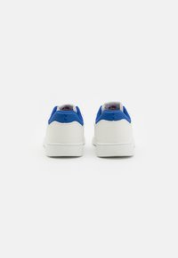 Ein Paar weiße Sneakers mit blauen Fersenkragen, von hinten betrachtet, vor einem schlichten weißen Hintergrund.