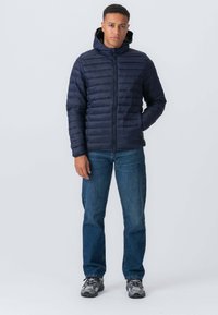 Marineblå dunjakke med lynlås foran og hætte, med quiltet design. Sæt sammen med blå jeans og grå sportssko.