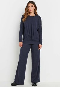 Navy blauwe gebreide lounge set met een losse lange mouw top met een geknoopt voorpand en wijde broekspijpen, zachte textuur en een relaxte pasvorm.