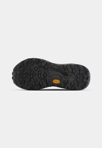 Semelle extérieure Vibram noire avec des bandes profondes, présentant un motif central lisse et un détail de logo doré, conçue pour la durabilité et l'adhérence.