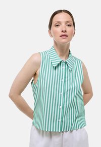 Blouse sans manches rayée verte et blanche avec col, dotée d'une fermeture à boutons et d'un ourlet droit. Tissu lisse et léger.