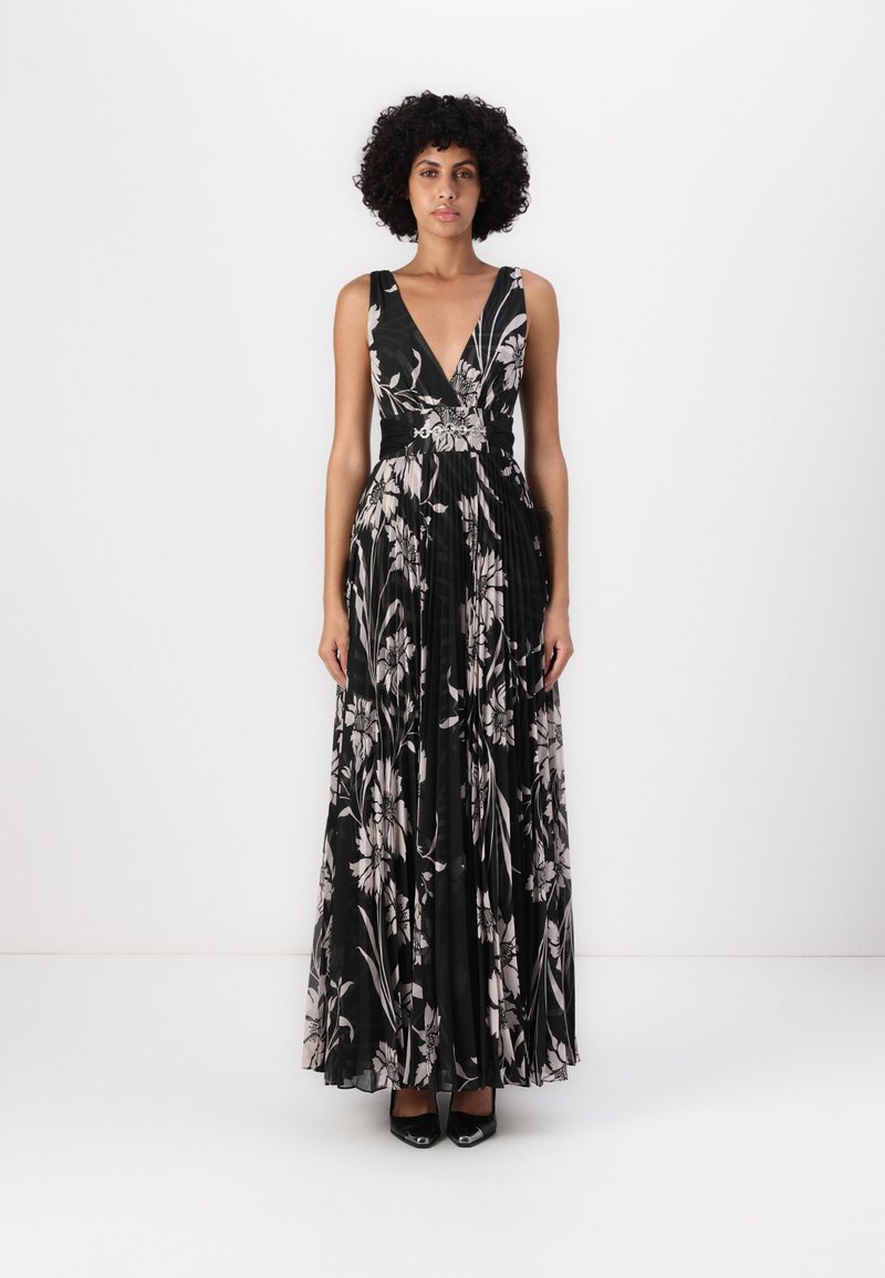 Robe maxi noire à fleurs avec un décolleté en V profond, un tissu plissé et une taille cintrée. Accessoirisée avec de l�égers motifs floraux et des talons noirs élégants.