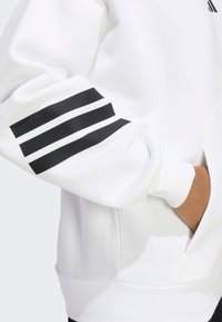 Biela mikina so čiernym trojprúžkom na rukáve, rebrovanými manžetami a predným vreckom. Hladká textúra, športový strih.