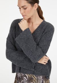 Grauer Strickpullover mit V-Ausschnitt, langen Ärmeln und strukturiertem Stoff. Hat eine lockere Passform und einen schrägen Schulterdesign.