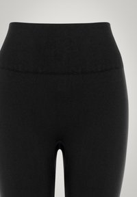 Leggings neri a vita alta realizzati in tessuto elasticizzato, con una fascia in vita liscia e un piccolo dettaglio a taglio nella parte anteriore.