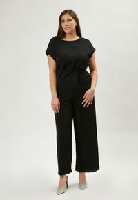 Top nero con maniche corte, scollo rotondo e lacci regolabili in vita, abbinato a pantaloni neri a gamba larga e tacchi alti scintillanti.
