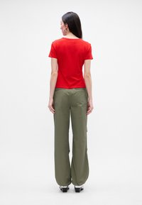 Crvena majica kratkih rukava u kombinaciji s maslinastozelenim hlačama širokog kroja, s opuštenim fit i glatkom tkaninom, prikazana sa stražnje strane.